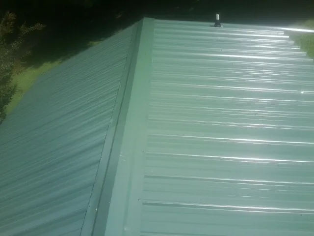 New green metal panels meeting at the ridge of a roof — Flat Roof Repair work by our crew in Forsyth